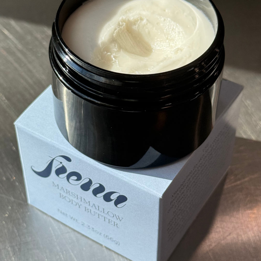 Open jar of marshmallow infused tallow body butter on top of Frena box it came in. 